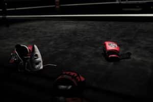 Boxing gloves and head gear lay on a boxing ring mat