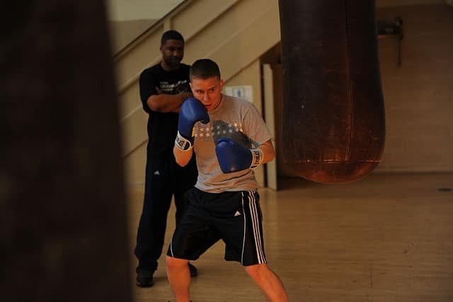 Boxer wearing beginner boxing gloves during a heavy bag workout with his coach